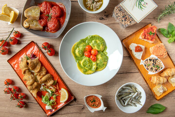 Italian food composition and seafood appetizers , with pesto ravioli stuffed with crab, bruschetta, codfish skewers, anchovies , meatballs with sauce, legumes over rustic wooden table background.
