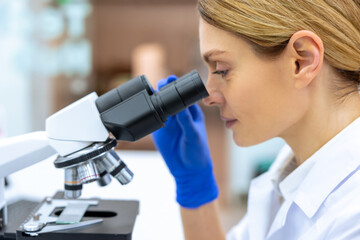 Professional lab. Profile portrait of blonde female medical worker using microscope during research.