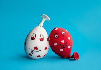 Two funny homemade sensory stress balls, made of balloons and filled with flour. Red and white balls with hearts and funny drawn faces on blue minimal background. - obrazy, fototapety, plakaty