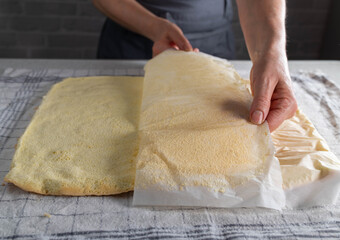 Removing baking paper from a fresh baked sponge cake for making swiss roll by a woman´s hand