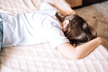 Upset lady in a white t-shirt lies on the bed.