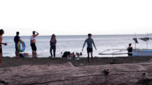 Young active people enjoy sunbathing on the sandy shore of cheap resort beaches at dawn during the hot summer. Driftwood obscures the view. Blurs, silhouettes