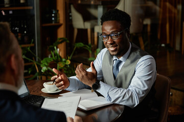 African American businessman discussing business plans with his partner while they sitting at table at meeting in cafe
