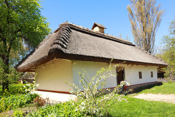 Fototapeta na wymiar Whitewashed house with a thatched roof from Middle Transnistria in skansen Pirogovo in Kyiv, Ukraine