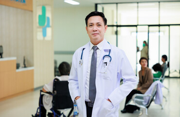 Asian male doctor in white uniform look at camera standing in patient reception at modern hospital. Healthcare medical and medicine concept.