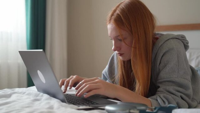 Young woman talking on smartphone while using laptop at home on bed. Teenage girl speaking with friends mobile phone working computer, studying typing, online shopping, watching video, Generative AI