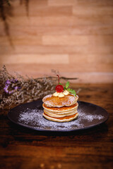 A stack of banana pancakes with slices of fresh bananas, walnuts and honey on top with cup of tea on a wooden background. A healthy breakfast. Copy space