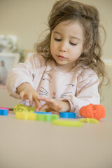 Caucasian child, two or three years old, playing and exercising fine motor skills with her hands, with clay and colored plasticine. Concept of happy childhood, learning and creativity. Copy space