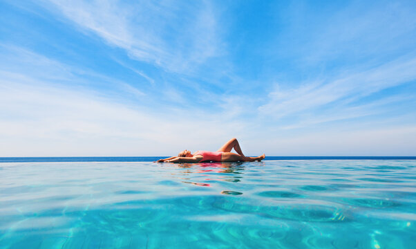 Happy girl have fun on summer beach holiday. Young woman relaxing at edge of infinity swimming pool with sea view from hill top. Healthy family lifestyle, summer travel with kids on tropical islands.