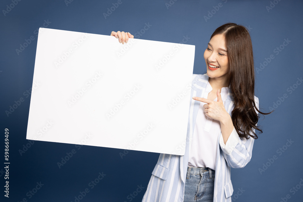 Wall mural young asian businesswoman in suit showing and holding blank white billboard isolated on blue backgro