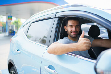 Happy cheerful Asian ale car driver waving or showing thumb up and smiling out of the car. Happy man waves a hand and smiles to camera close up with copyspace. Safety driving and insurance concept.