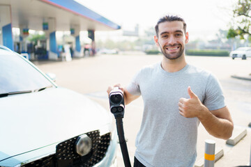 Cheerful happy Asian man using an EV charging application on smartphone to prepare vehicle charging and payment. Modern lifestyle of transportation with sustainability and sustainable energy.