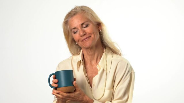 Closeup of beautiful smiling happy blond mature woman holding wineglass and drinking coffee or tea looking to the side on solid white background with copy space Generative AI
