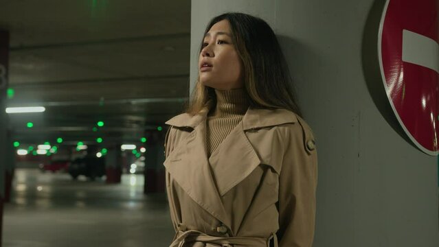 Frightened Asian ethnic chinese korean woman hiding from danger pursuit threat phobia in underground shelter night dark car parking scared fearful girl stand alone near stop driving Generative AI