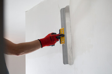Leveling the walls with white putty - the hands of a master with a spatula
