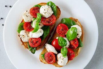 Caprese Bruschetta with fresh tomatoes, mozzarella and Basil leaves on light background. Vegetarian food. Top view