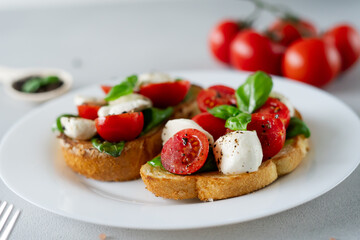 Close-up of Bruschetta with tomatoes, mozzarella and basil leaves on light background. Crostino Caprese