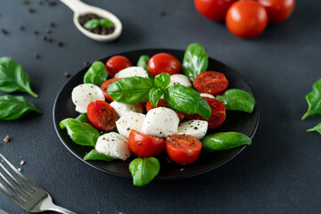 Caprese salad with ripe tomatoes and mozzarella cheese with fresh basil leaves on black background. Italian food