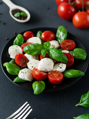 Caprese salad with ripe tomatoes and mozzarella cheese with fresh basil leaves on black background. Italian food