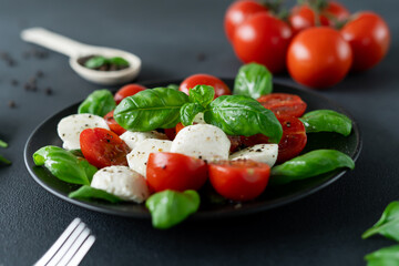 Italian Caprese salad with sliced tomatoes, mozzarella cheese, basil, olive oil on black background. Vegetarian food