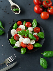 Italian Caprese salad with sliced tomatoes, mozzarella cheese, basil, olive oil on black background. Vegetarian food