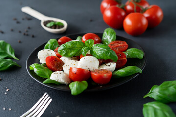 Italian Caprese salad with sliced tomatoes, mozzarella cheese, basil, olive oil on black background. Vegetarian food