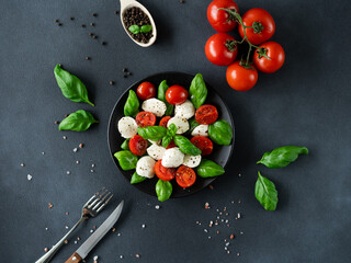 Top view of Caprese salad with sliced tomatoes, mozzarella cheese, basil, olive oil on black background. Vegetarian food