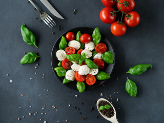 Caprese salad with ripe tomatoes and mozzarella cheese with fresh basil leaves on black background. Italian food. Top view