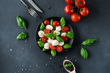 Top view of Caprese salad with ripe tomatoes and mozzarella cheese with fresh basil leaves on black background. Italian food