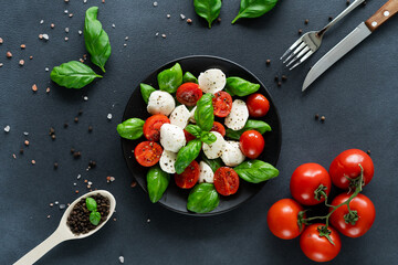 Top view of Caprese salad with ripe tomatoes and mozzarella cheese with fresh basil leaves on black...