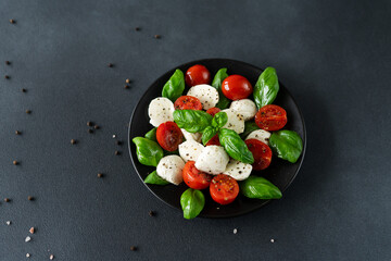 Caprese salad with ripe tomatoes and mozzarella cheese with fresh basil leaves on black background. Italian food
