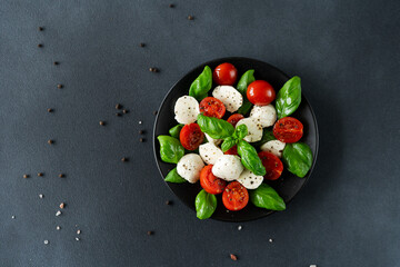 Top view of Caprese salad with ripe tomatoes and mozzarella cheese with fresh basil leaves on black background. Italian food. Copy space for text