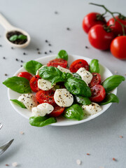 Italian Caprese salad with sliced tomatoes, mozzarella cheese, basil, olive oil on light background. Vegetarian food