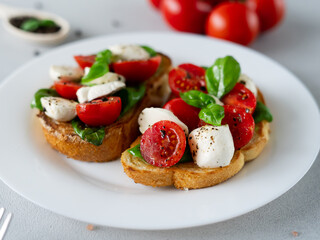 Bruschetta with tomatoes, mozzarella and basil leaves on light background. Crostino Caprese