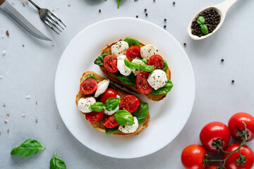Caprese Bruschetta with fresh tomatoes, mozzarella and Basil leaves on light background. Vegetarian food. Top view