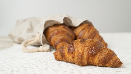 Croissant in linen eco bag. Cotton bag with croissants on wooden background.