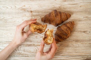 Hands tearing a fresh croissant. Croissants turn apart. Croissant in wooman hand on wooden table.