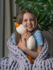 Cheerful, teenage girl with long hair, wrapped in a plaid with a large knit. she has a toy goose in her hands
