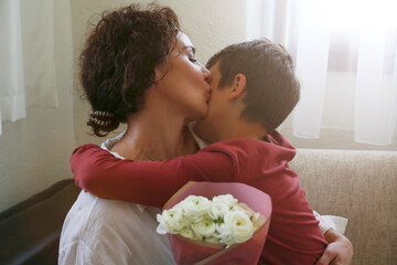 Son giving his mom a bouquet of ranunculus flowers for mother's day. Adorable scene with a tween boy surprizing his mum with a present. Close up, background, portrait.