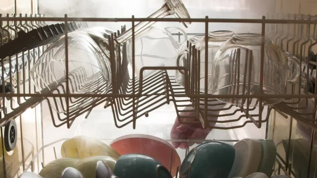 Sterilization of Dishes. View from the dishwasher to the outside. The door opens and clouds of steam burst out, illuminated by a bright light. Filmed at a speed of 120fps