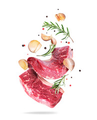 Two raw beef steaks with rosemary and garlic cloves in the air isolated on a white background