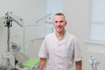 Naklejka na ściany i meble portrait of a handsome young smiling dentist doctor standing in the dental office before starting the procedure