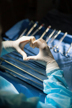 the doctor shows the heart sign with his hands after the operation on the background of surgical instruments