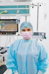 Portrait of a young female doctor in a mask and sterile protective clothing standing in the operating room after an operation