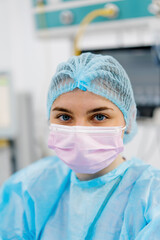 Portrait of a young female doctor in a mask and sterile protective clothing standing in the operating room after an operation