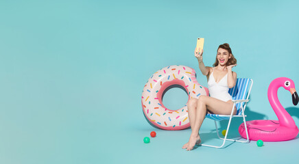 Happy woman chilling in deck chair near rubber ring taking selfie photo looking at smartphone on blue copy space background. woman relaxing on beach in summer holiday.