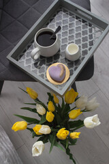 Start the morning with coffee and a bouquet of tulips. A tray with coffee and cake on a chair near  flowers