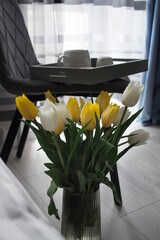 A tray with coffee and cake on a chair near panoramic window. Beautiful yellow and white tulips for magazine cover