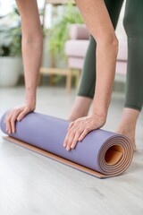 Blonde woman rolling up her yoga mat after a practice at home