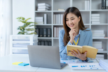 Charming Asian businesswoman working with a laptop at the office. Happy young Asian businesswoman sitting at desk and take notes with laptop computer in the office.